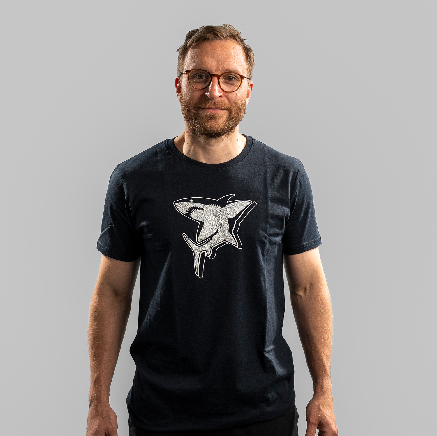 Navy-blaues T-Shirt der Kölner Haie mit großem Frontprint des Hais aus dem Kölner Haie-Logo. Getragen von Frederik Storm, Frontansicht, vor hellem Hintergrund.
