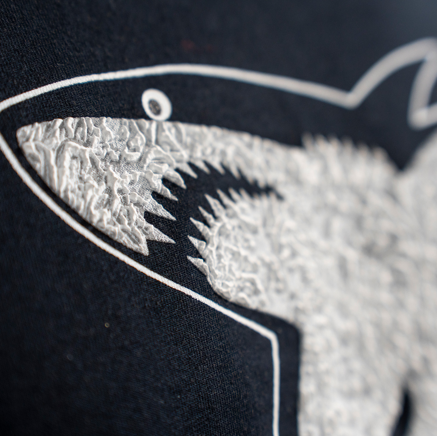 Detailansicht 3D-Druck vom Haie-Logo auf navy-blauen T-Shirt.