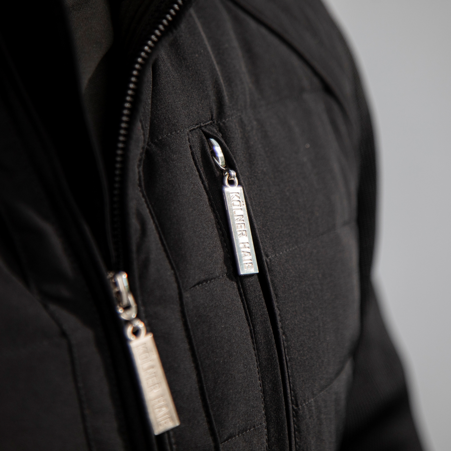 Detailansicht der silbernen Zipper für Jacke und Brusttasche der schwarzen Kölner Haie Jacke.