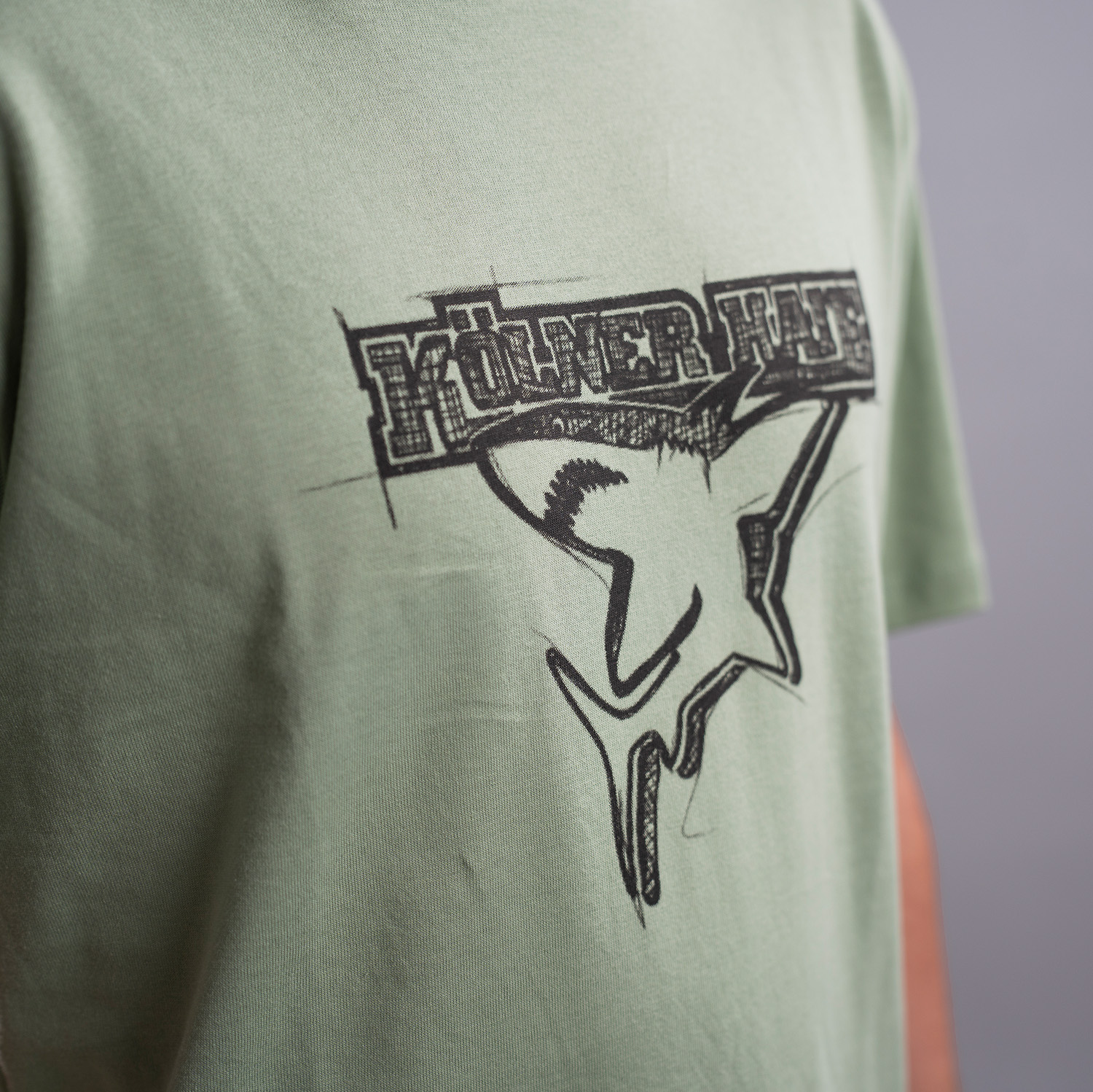 Detailansicht Druck Kölner Haie Logo auf grünem T-Shirt. Das Logo ist skizzenhaft gedruckt.