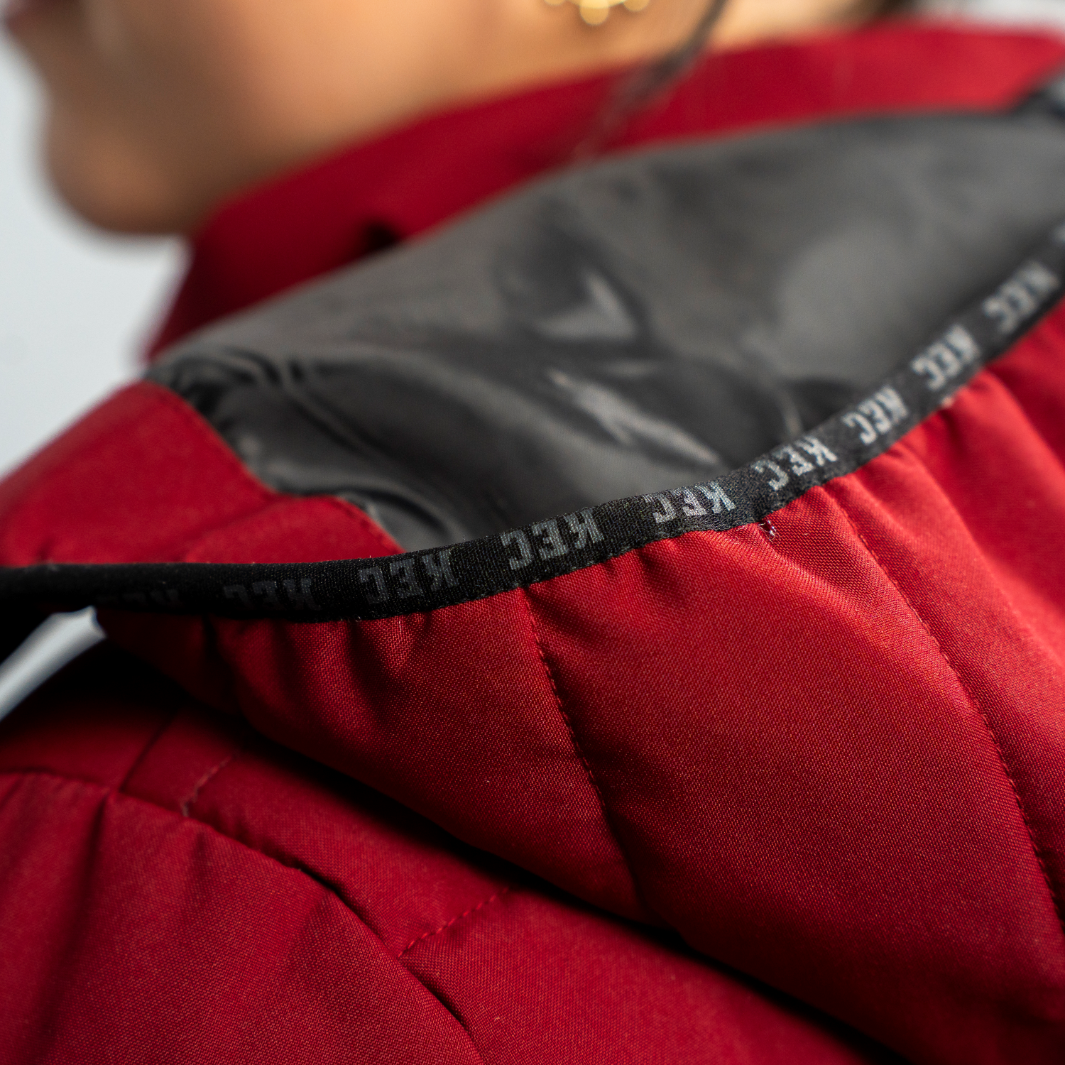 Detailansicht Kapuze mit KEC Schriftzug auf abgesetztem schwarzgrauen Stoff der bordeauxroter Jacke.