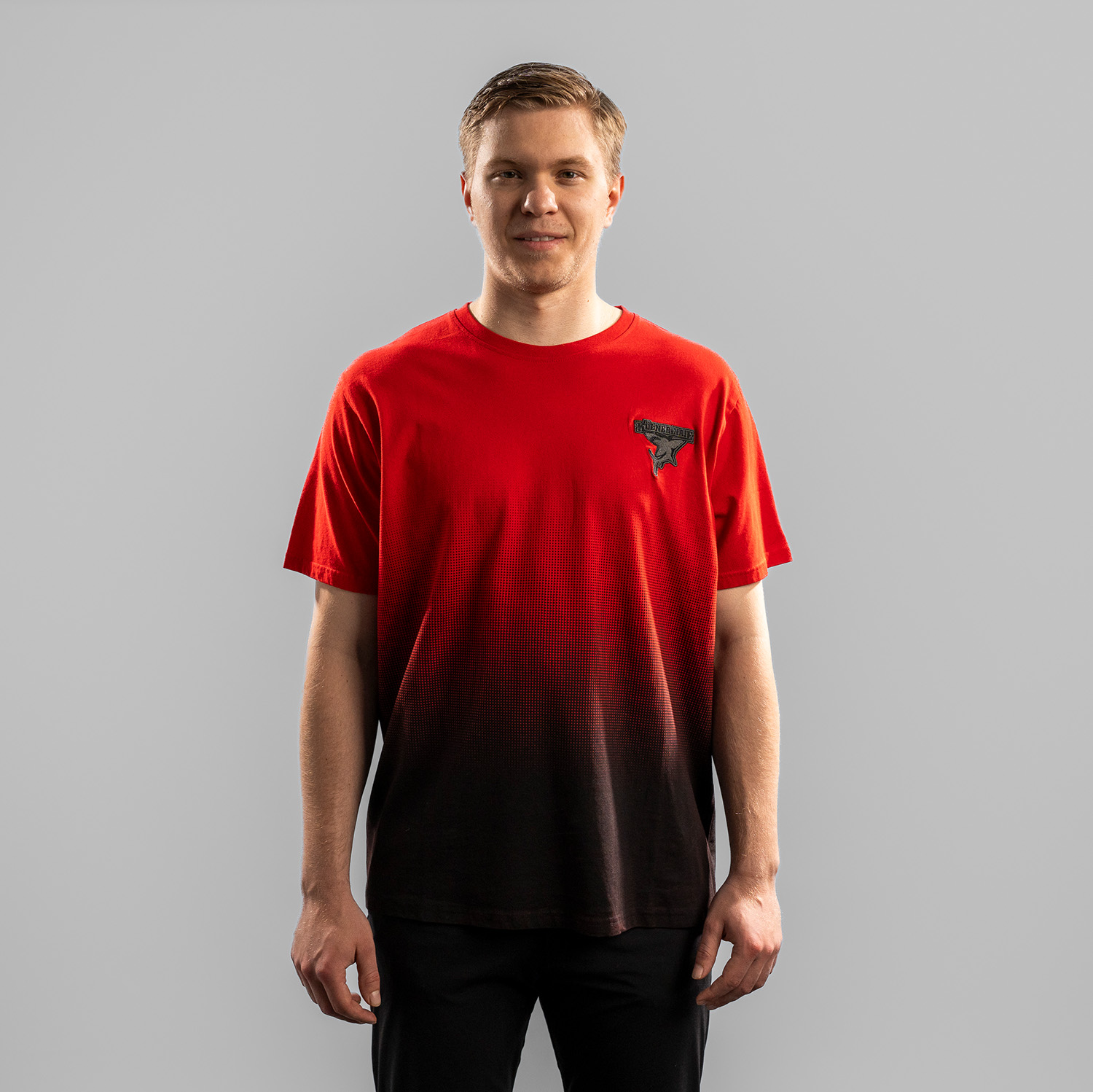Rotes T-Shirt mit Verlauf ab Brustbereich nach unten zu Schwarz der Kölner Haie mit grau gesticktem Kölner Haie Logo auf der linken Brust (Herzseite), getragen von Tobi Ancicka, Frontansicht vor hellem Hintergrund.