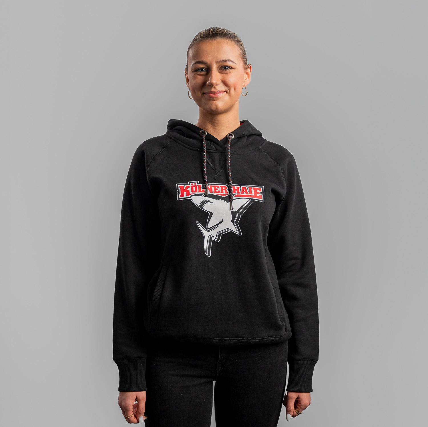 Schwarzer Damen Hoodie mit großem Frontprint vom Kölner Haie-Logo, getragen von Model, Frontansicht, vor hellem Hintergrund.