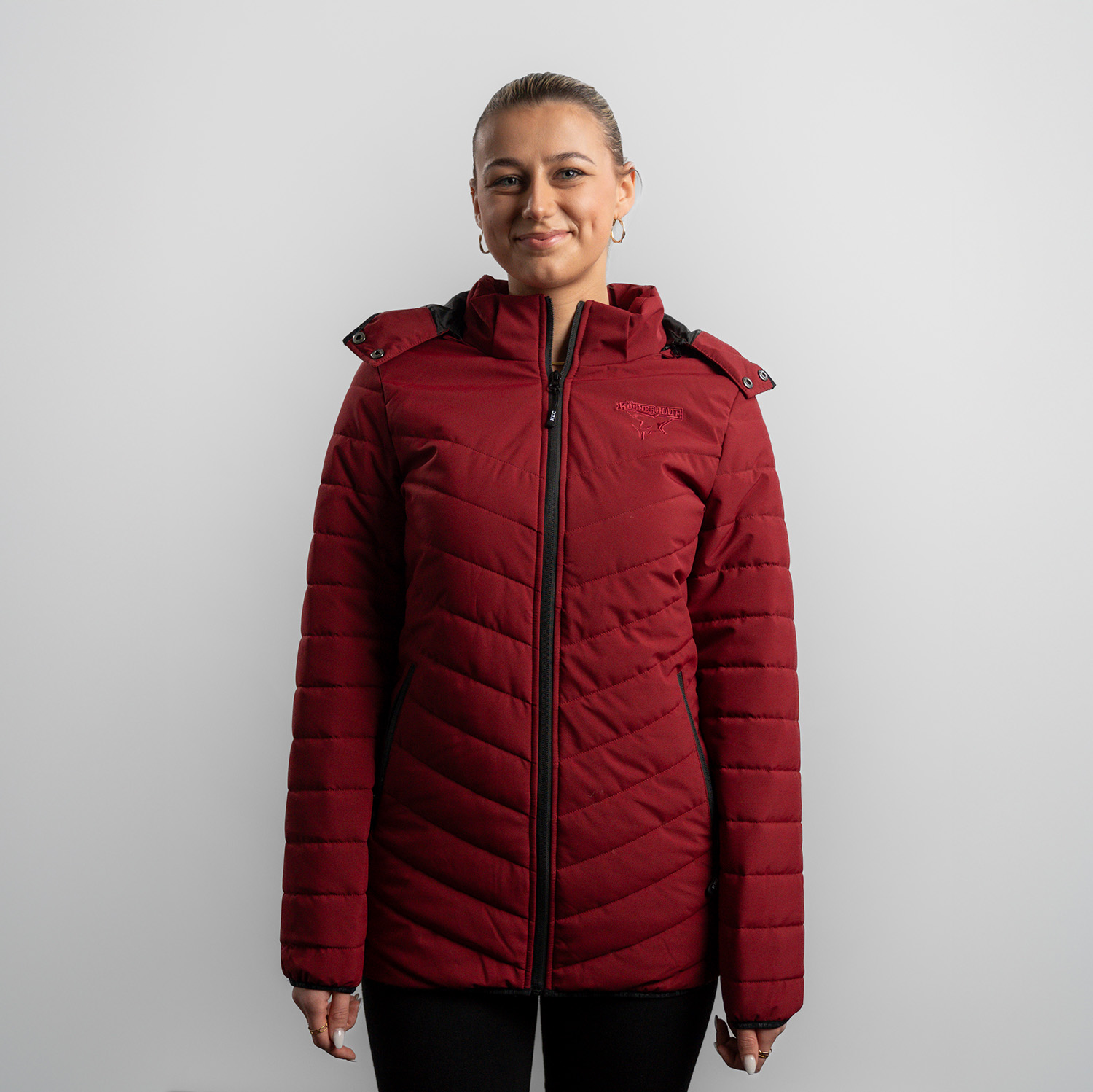 Steppjacke PETRA Bordeauxrote Damen Steppjacke mit abnehmbarer Kapuze, dezentes Ton-in-Ton Kölner Haie-Logo auf linker Brust (Herzseite) und zwei Eingrifftaschen, getragen von Model, Frontansicht, vor hellem Hintergrund.