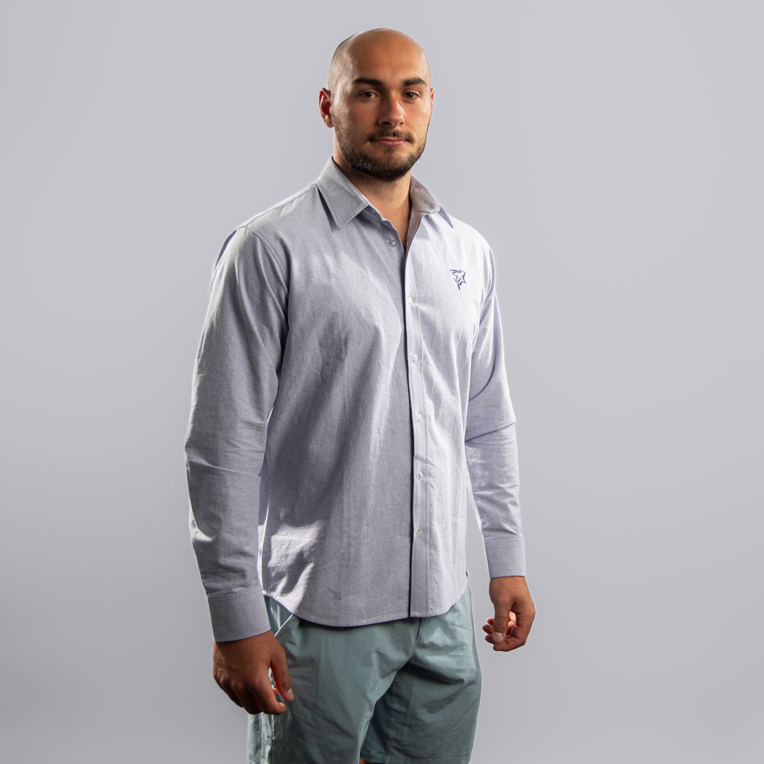 Hellblaues Hemd mit dezentem Button-Down-Kragen und dunkelblauer Haie-Stickerei (Shark-Logo) auf der linken Brustseite. Getragen von Maxi Glötzl, Frontansicht mit leichter Schultereindrehung, rechte Schulter vorne, vor hellem Hintergrund.