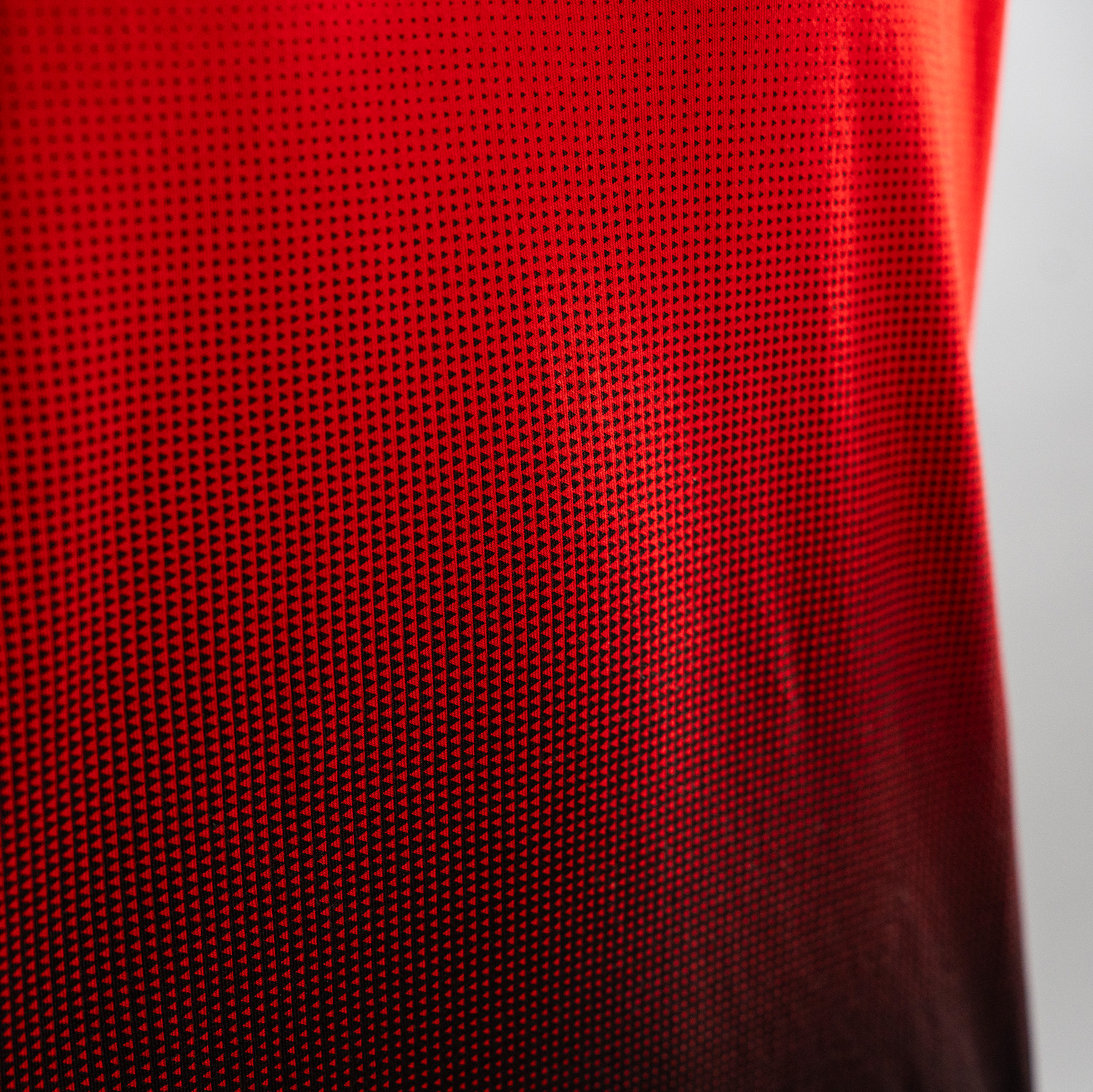 Detailansicht rotes T-Shirt mit Verlauf ab Brustbereich nach unten zu Schwarz. Verlauf entsteht durch gedrucktes Muster von Dreiecken. Von oben nach unten werden kleine schwarze Dreiecke immer größer und enden im schwarzen unteren Teil des T-Shirts. Ander