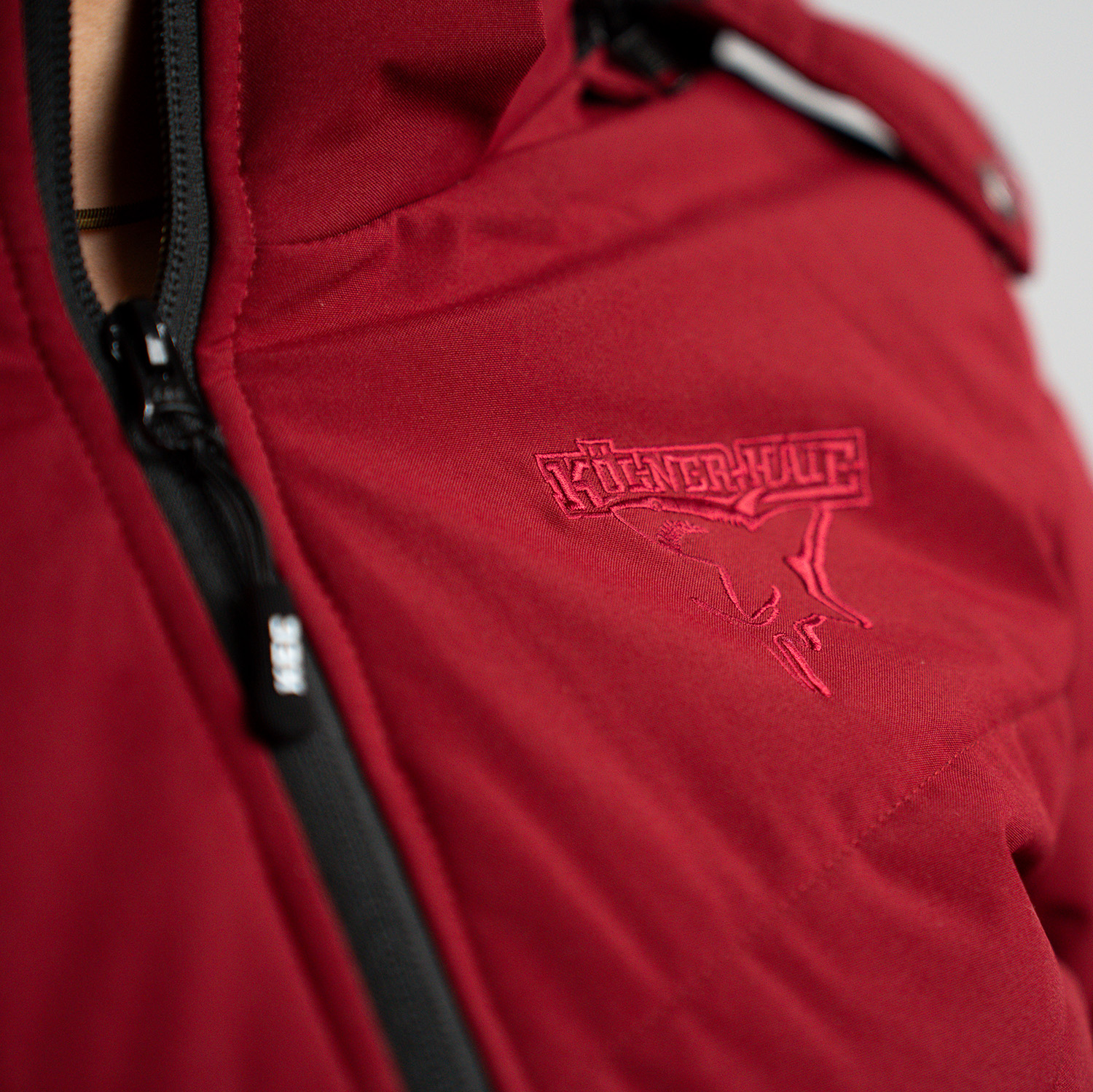 Detailansicht gesticktes Ton-in-Ton Kölner Haie-Logo auf linker Brust auf bordeauxroter Jacke.