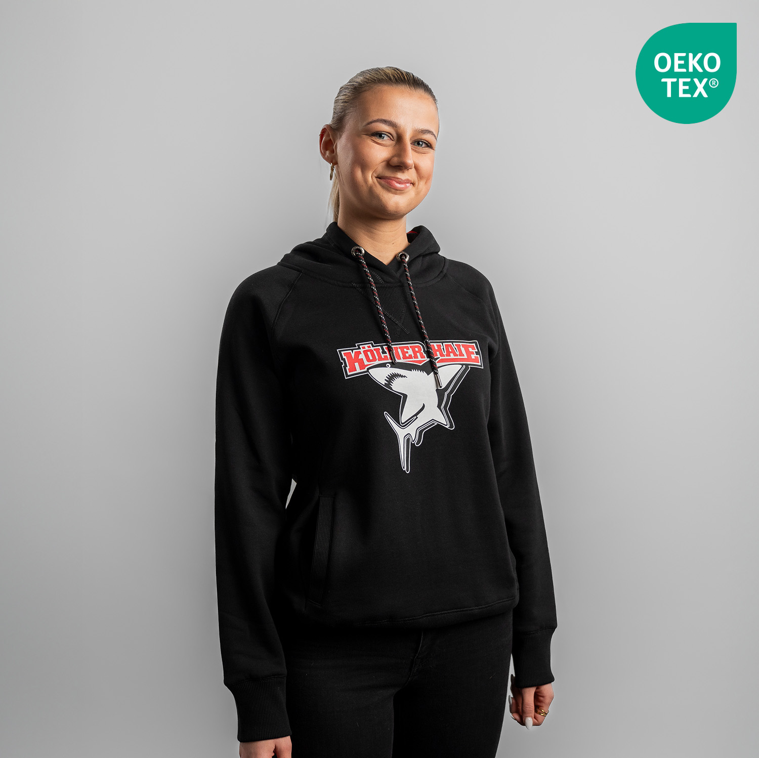 Schwarzer Damen Hoodie mit großem Frontprint vom Kölner Haie-Logo, getragen von Model, Frontansicht, vor hellem Hintergrund.
