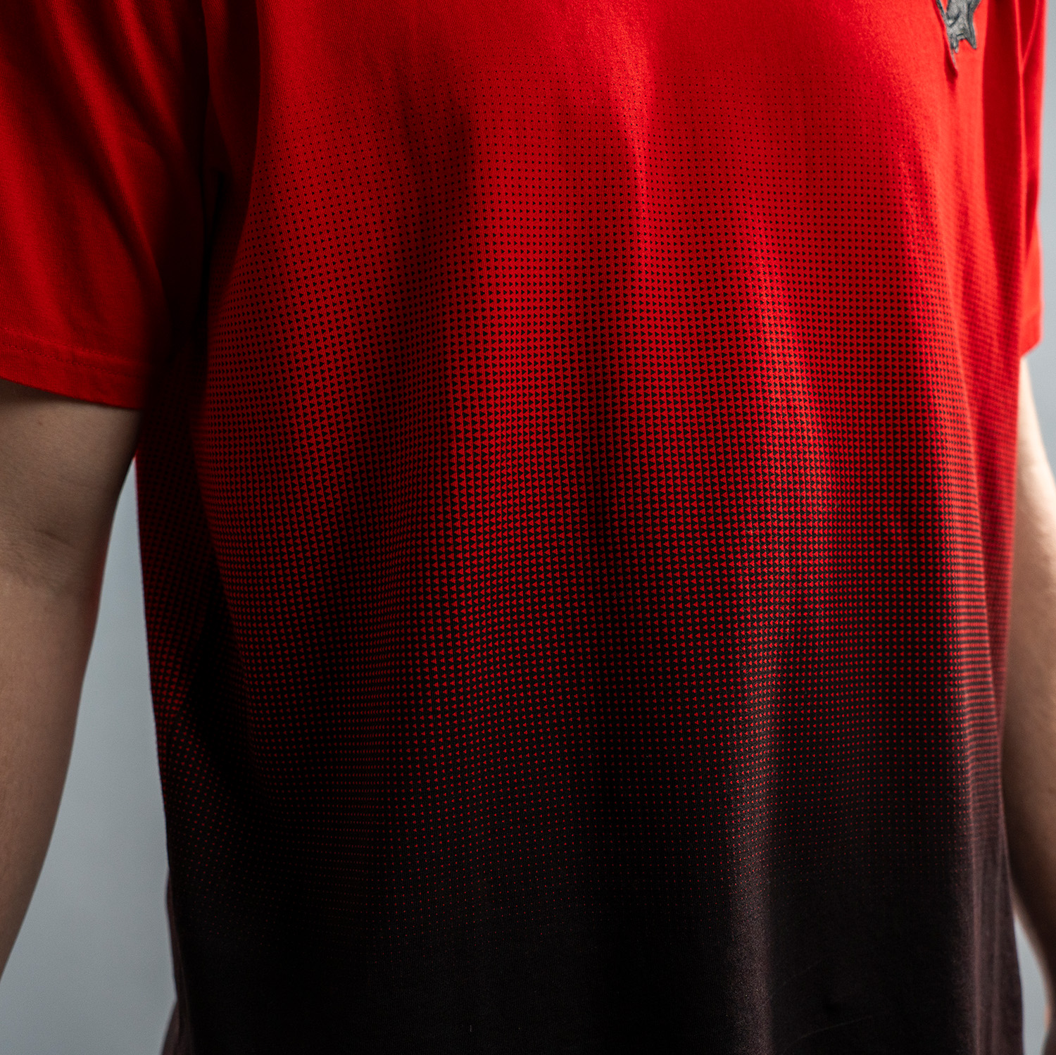 Detailansicht rotes T-Shirt mit Verlauf ab Brustbereich nach unten zu Schwarz. Verlauf entsteht durch gedrucktes Muster von Dreiecken. Von oben nach unten werden kleine schwarze Dreiecke immer größer und enden im schwarzen unteren Teil des T-Shirts. Ander